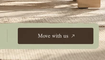 Close-up of a dark brown Move with us button with a small arrow, at the end of a sage bar over a woven rug.