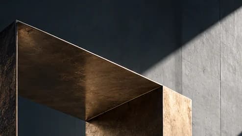 Close-up of the top of a bronze portal, its inner face lit gold by a diagonal beam of sunlight on concrete.