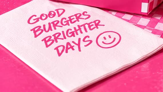 White napkin hand-lettered in pink with GOOD BURGERS BRIGHTER DAYS and a smiley, on a pink Bah tray