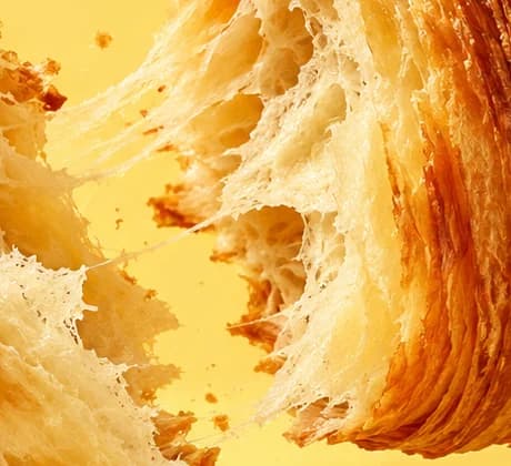Extreme close-up of a croissant torn in two, its open honeycomb crumb and stretched strands of dough.