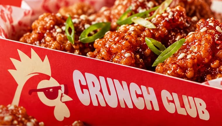 Red takeaway box printed with a cream rooster in red sunglasses and CRUNCH CLUB, glazed chicken piled inside.
