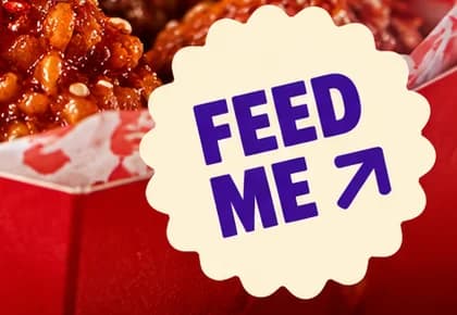Scalloped cream sticker reading FEED ME in violet capitals with a diagonal arrow, over the chicken box.