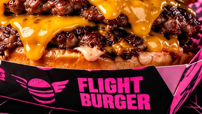 Black Flight Burger wrapper with the winged mark and pink lettering, under a dripping double smash burger