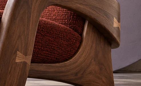 Close-up of the walnut armchair frame with two pale bow-tie joints beside rust woven upholstery