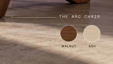Label 'THE ARC CHAIR' in monospaced capitals above round walnut and ash wood swatches on a polished floor