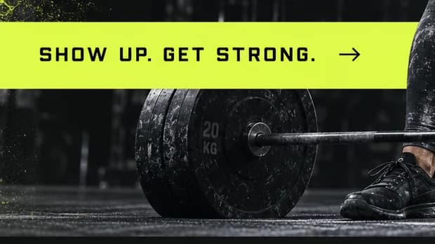 Close-up of a lime band reading SHOW UP. GET STRONG. with an arrow, above a black 20 kg bumper plate.