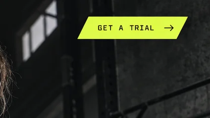Close-up of the top right corner: a slanted lime GET A TRIAL tab with an arrow, over dark gym windows.