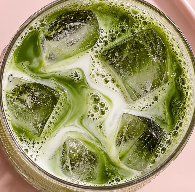Top-down close-up of an iced matcha latte, green and white marbling around ice cubes in a ribbed glass.