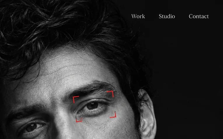 Close-up of a black-and-white face, a red camera focus frame on one eye, under the links Work, Studio and Contact.