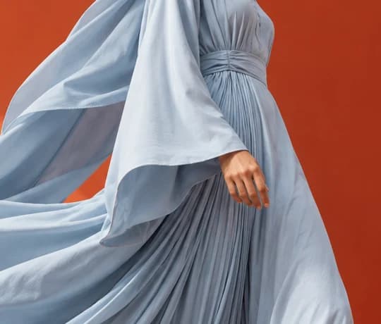 Close-up of the powder blue abaya: wide sleeve, wrapped sash and fine pleats against a burnt-orange wall