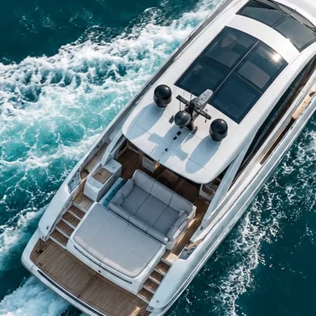 Close-up of the white motor yacht from above: flybridge, cushioned aft lounge and teak deck over teal water
